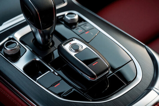 Close up of modern car ignition key and gear shift lever inside luxury vehicle interior. Shiny chrome accents and red leather seats visible.