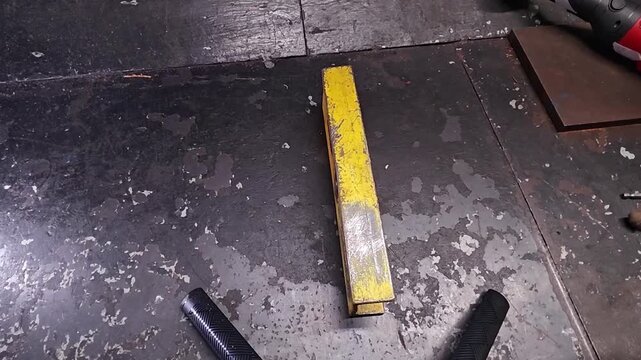 Spirit level marks drilling alignment on heavy steel panels. Yellow measuring tool lies across metal while drill hardware waits nearby, suggesting careful workshop preparation and accuracy.