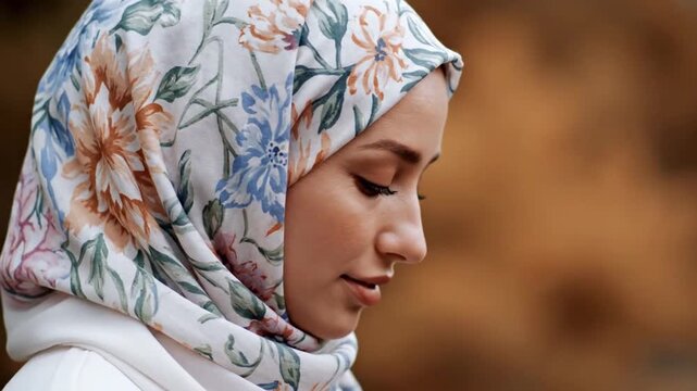 Profile of young Muslim woman wearing floral hijab looking down thoughtfully.
