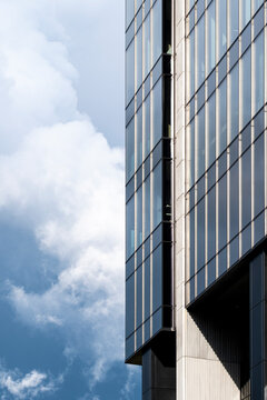 Modern building facade rising beside open sky and clouds with clean vertical architecture and geometric lines emphasizing height and minimal urban design