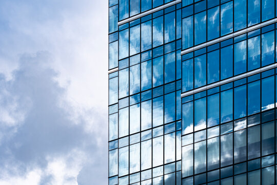 Blue glass building facade reflecting clouds and sky through geometric windows in modern architecture with a clean vertical rhythm and open negative space