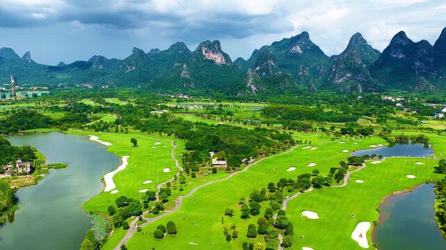 High angle view of an expansive green golf course with ponds and sand traps set against dramatic karst mountains in Guilin, Guangxi, China.