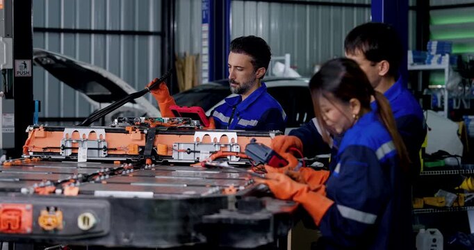 Three EV technicians test exposed battery pack with meters and probes, moving leads across components and comparing diagnostic readings during high voltage battery inspection in modern workshop.