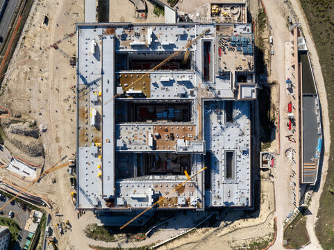 Aerial view of a large rectangular building under construction with multiple cranes, construction materials, and surrounding dirt ground in Ancona, Marche, Italy.
