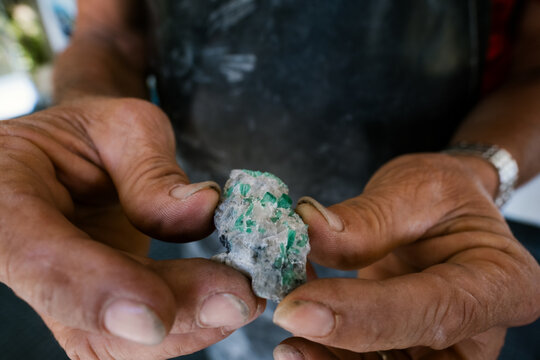 Hands holding raw emerald crystal gemstone mineral ore