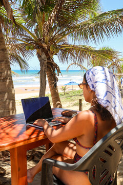 Remote worker typing under coconut palms by the sea