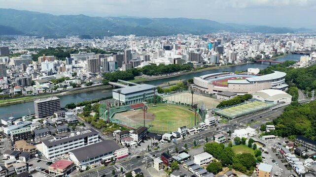Aerial drone footage over urban cityscape with baseball stadium in Kochi, Japan