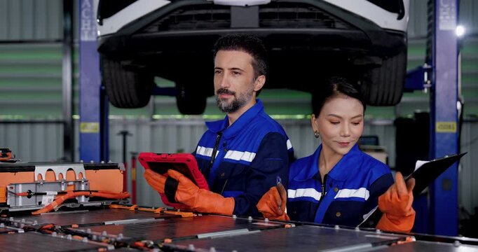 Digital EV battery diagnostics with male and female technicians reviewing tablet data beside exposed battery system, supporting technical inspection and preventive maintenance in modern workshop.