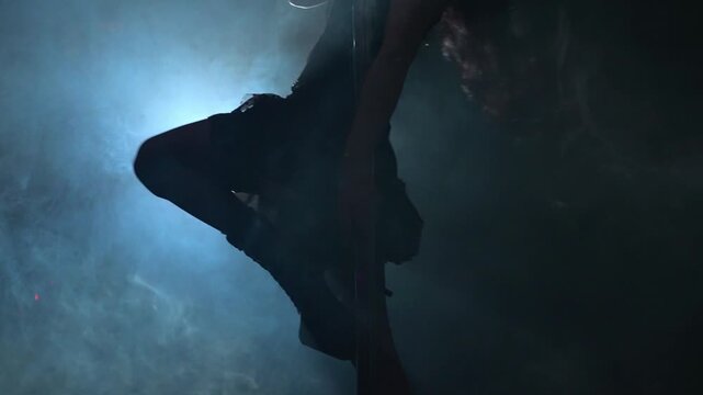 Pole dancer silhouette in backlit smoke on stage.