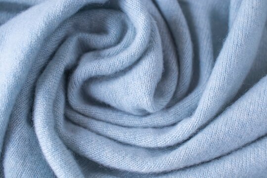 Soft blue cashmere fabric with folds and ripples. Background with a soft, light-blue knit texture.