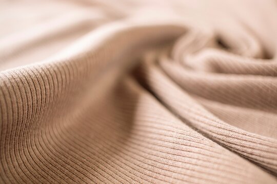 Beige ribbed cotton fabric falling in soft folds. Textured, draped beige ribbed fabric (close-up view).