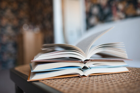 Stack of open paper boos on rattan table in living room close up. Reading hobby.