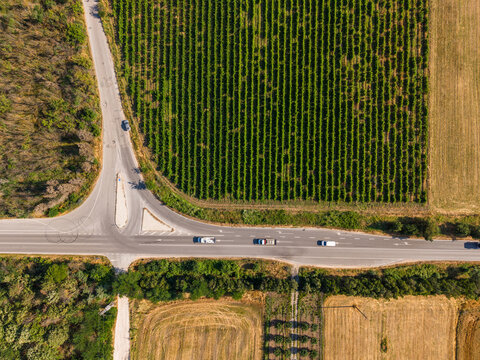 Aerial view of a T-junction road intersection surrounded by lush agricultural fields and trees in Varna, Bulgaria.