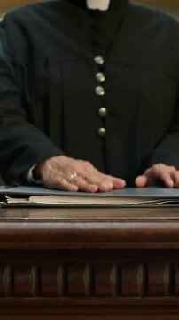 Vertical video: Holding closed folder then priest smoothing papers on table for service with collar