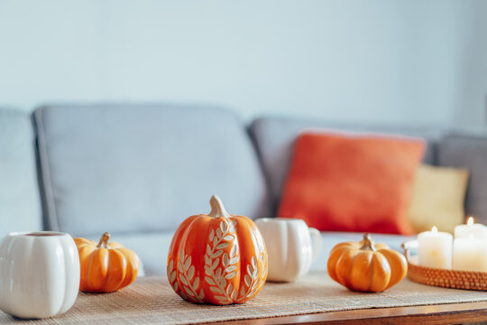 Autumn fall mood composition for hygge home decor. Hot tea or coffee drink in pumpkin's shaped cups, pumpkin decor and burning candles on the coffee table. Festive autumn, fall mood home decor