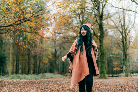 Young Woman wrapped in warm Shawl Poncho enjoying autumn walk in forest with fall yellow leaves. Travel lifestyle. Feeling harmony, reunion with nature. Relaxing, mental recovery. Local travel.