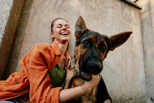Laughing woman hugging her happy dog against concrete wall. Concept of friendship, love, and joy between pet and owner. Warm natural light creates a cheerful, candid mood.