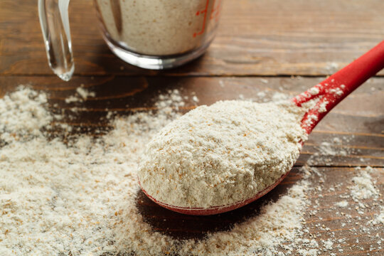 Scoop of whole wheat flour on a rustic wood illustrating baking ingredients and natural food preparation.