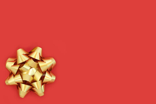 Gold ribbon gift bow for present, birthday, anniversary, greeting card, gift tag, label. Decorative contrast art abstract design. On red background, copy space.
