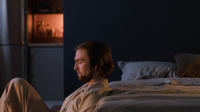 Caucasian young adult man wearing headphones, listening to music on vintage CD player and resting on bed. Ideal for music commercials, stress relief campaigns and evening wellness content