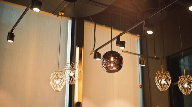 Multiple light fixtures are suspended in a contemporary indoor setting, featuring a mix of round and crystal designs. Natural light filters through nearby windows, creating a bright atmosphere