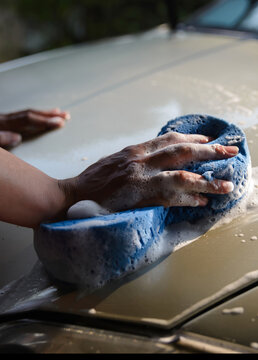 Car cleaning with sponge and soap, hand washing vehicle exterior for car wash, auto care and maintenance, showing foam and suds on automotive surface during manual cleaning-vertical image.
