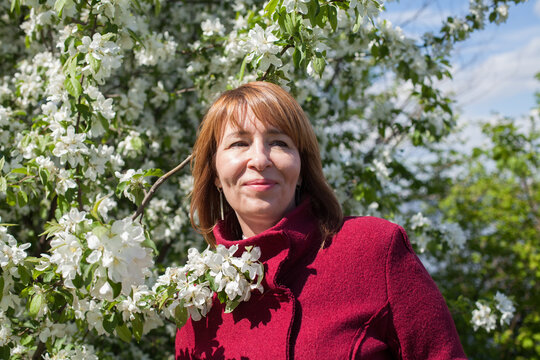 Cute mid adult woman in park on fresh spring flowers and green leaves background