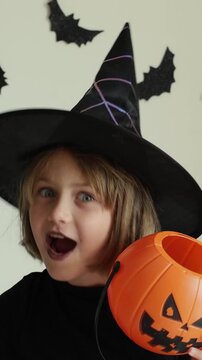 Video vertical portrait happy excited face girl trick or treat Halloween surprise kid wearing dress witch hat costume party Halloween.Toddler holding pumpkin jack lantern basket candies trick treating