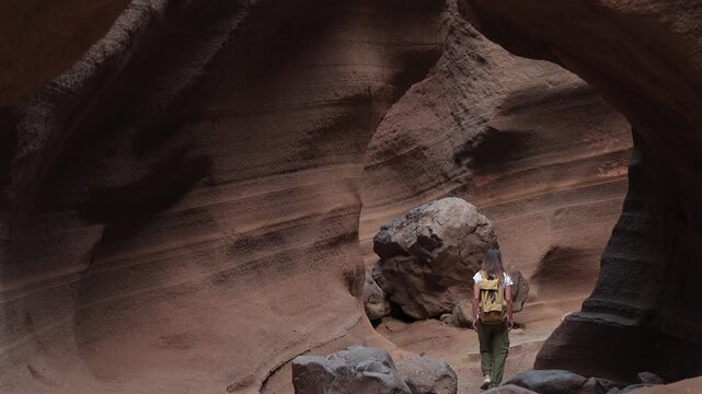 Woman with a backpack walking through a narrow slot canyon. Adventurous hiker exploring the geological formations of the Barranco de las Vacas