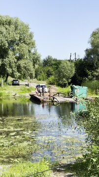 Manual vehicle ferry crosses the Sula River carrying cars across calm water through a rural landscape in Poltava region, Ukraine
