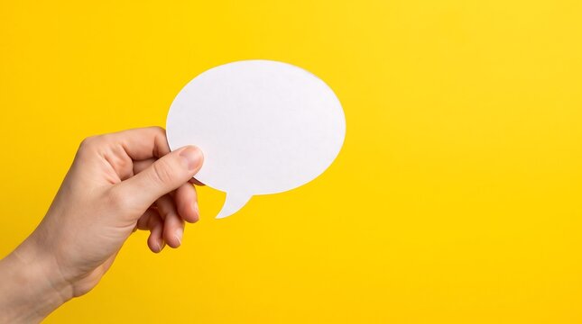 Hand holding a blank white speech bubble against a vibrant yellow background for communication concepts