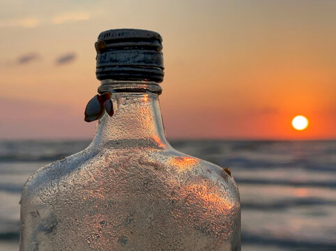 glass bottle with metal lid washed up on a beach, with sunrise in the background
