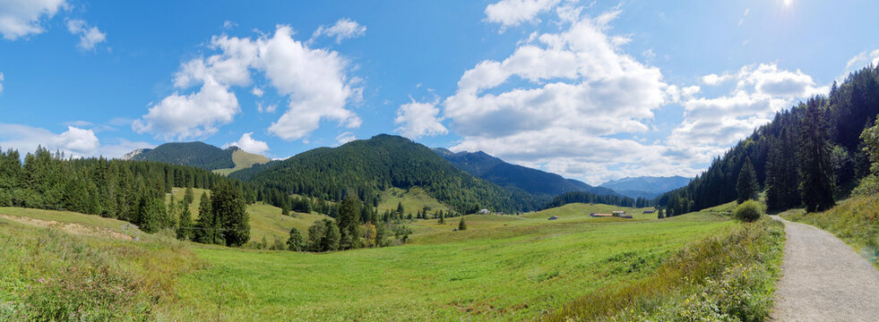 Bavarian landscape northwest of Spitzingsee resort. Rosskopf trail bordered by green pastures at the foot of the Rosskopf mountain, facing the Sonnenjoch on horizon 
