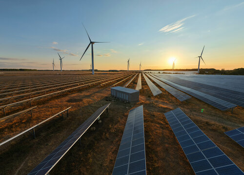 Aerial view of Chelveston Renewable Energy solar farm and wind turbines at sunset with rows of photovoltaic panels and rotating blades in Chelveston, England, United Kingdom.