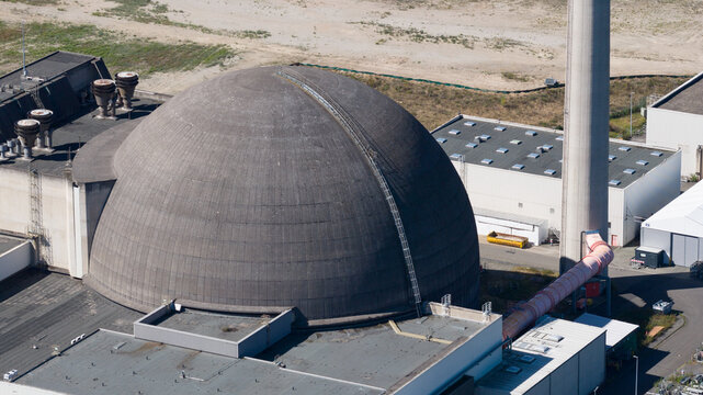 Aerial view of the large concrete dome of a nuclear power plant facility with an adjacent chimney and industrial buildings in Urmitz, Rhineland-Palatinate, Germany.