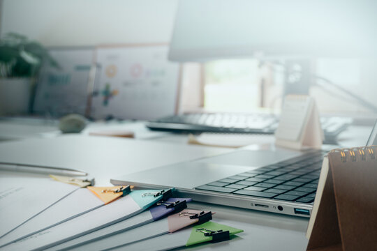 Modern office desk with laptop, organized paperwork with colorful binder clips, and calendar, concept of remote work, corporate administration, and business productivity.