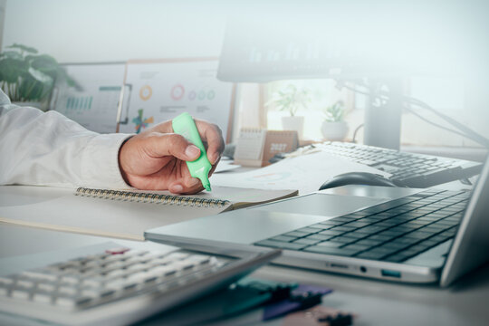 Businessman using a green highlighter to mark notes in a notebook on office desk with calculator and laptop, concept of business planning, strategy, and corporate work.
