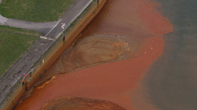 Aerial view of the Dormagen-Bayerwerk industrial site showing reddish water runoff along the concrete riverbank in Koln, Nordrhein-Westfalen, Germany.