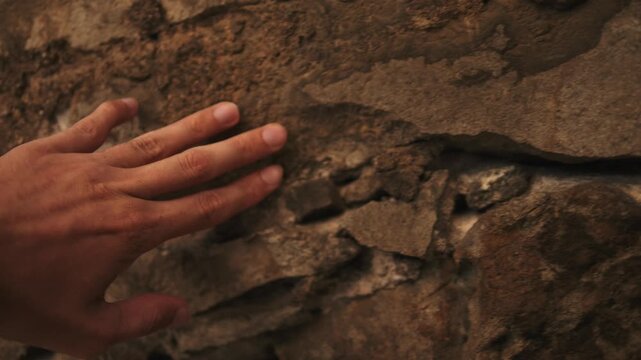 Hand touching the weathered stone wall of an old castle in Spain. Concept of history, travel, heritage and connection with the past.