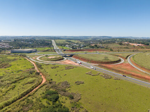 Aerial view of a highway interchange surrounded by green fields and red soil in the countryside of Brazil.