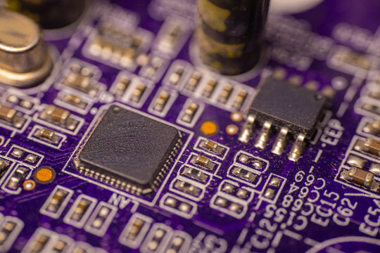 Close-up view of a purple printed circuit board featuring various electronic components including microchips, capacitors, and soldered connections