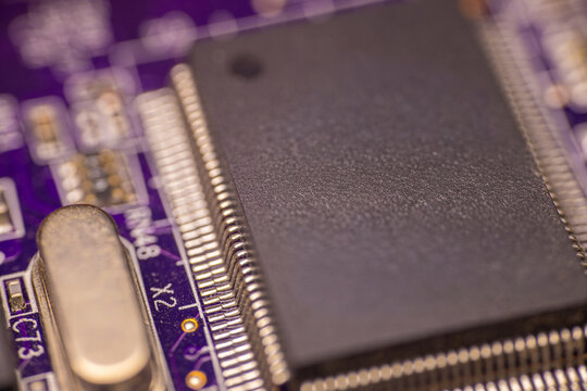 Close-up view of a black microchip mounted on a purple printed circuit board with metallic connectors and intricate circuitry details visible in the background