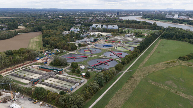 Aerial view of the Stammheim wastewater treatment plant with circular sedimentation tanks and industrial facilities near the Rhine river in Cologne, North Rhine-Westphalia, Germany.