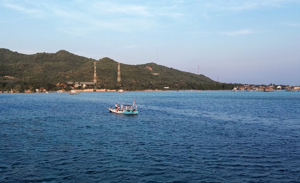 Aerial view of a small boat sailing on the blue waters of Karimunjawa National Park with lush green hills and communication towers in the background in Karimunjawa, Central Java, Indonesia.