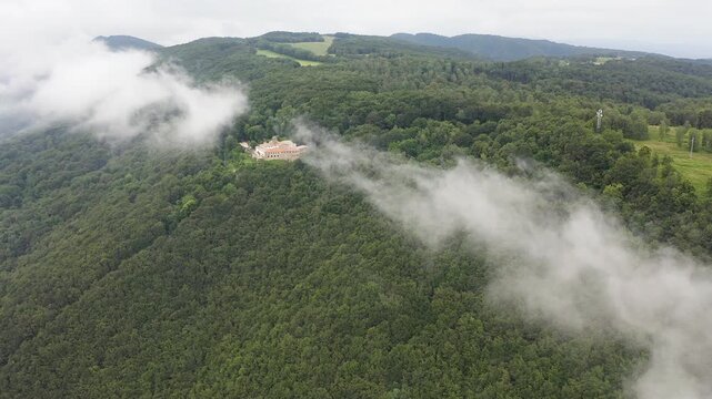 Aerial view of Mare de deu de la salut Hermitage, dramatically perched on a rocky cliff above dense forests, overlooking the beautiful mountain landscapes of Girona, Catalonia. 