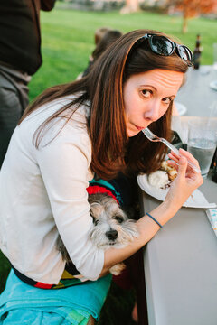 Woman Eating with Dog on Lap