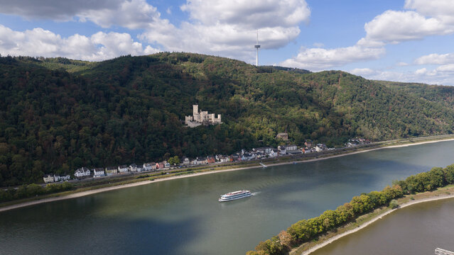 Aerial view of Stolzenfels Castle perched on a forested hill overlooking the Rhine river with a cruise ship sailing past the town of Koblenz, Rheinland-Pfalz, Germany.
