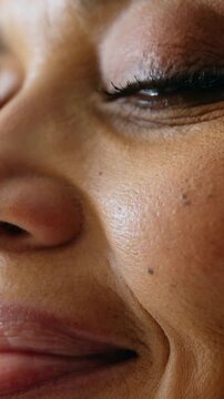 Vertical video: Smiling woman showing small blink triggered by smile in tight close-up, cheek mole