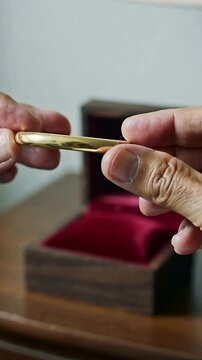 Vertical video: Lid lifting hands removing gold bangle from jewel box on table checking red velvet