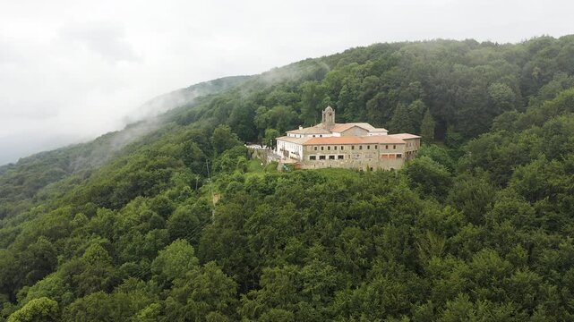 Aerial view of Mare de deu de la salut Hermitage, dramatically perched on a rocky cliff above dense forests, overlooking the beautiful mountain landscapes of Girona, Catalonia. 